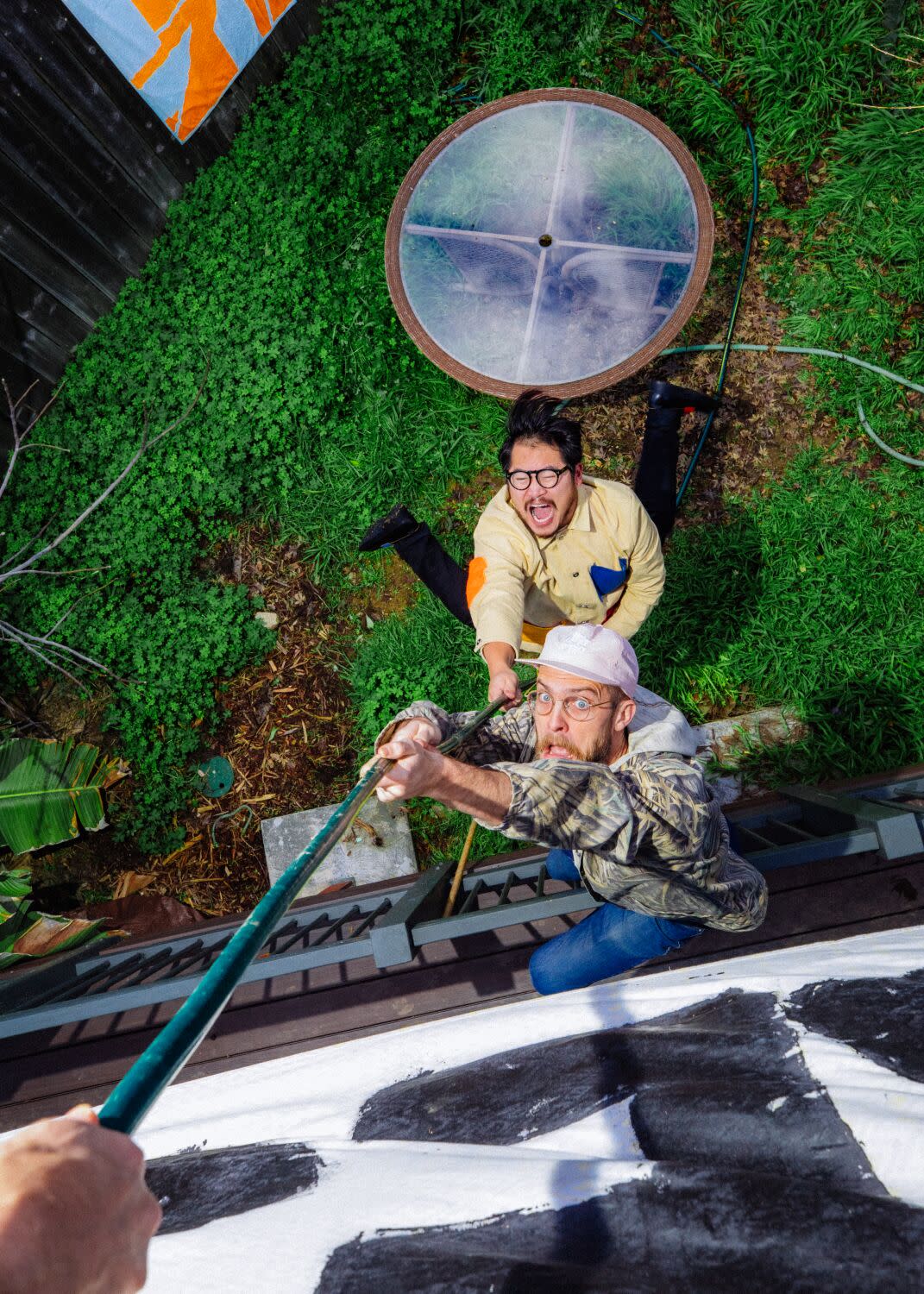 Two men pretend to be getting hoisted up the side of a house with a garden hose.