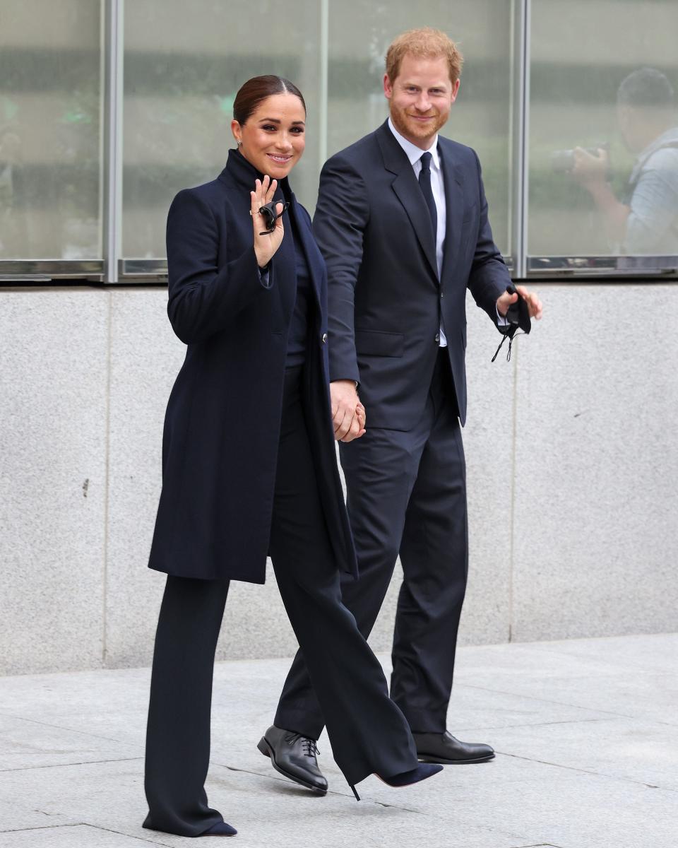 Meghan in an all black long coat, top, pants, and heels, and Harry in a dark grey suit.