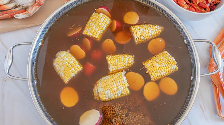 Corn cops and potatoes in seasoned water in pan with crab