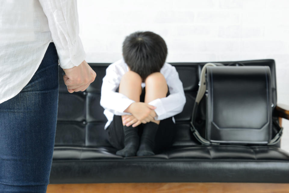 A child scrunched up into a ball sitting on a bench, as an angry adult confronts them. (Photo via Getty Images)