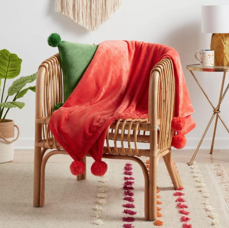 Orange throw blanket with pompoms draped over wicker chair