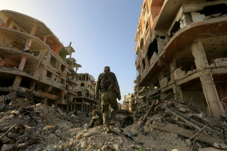 Syrian government forces walk down a destroyed street at the Palestinian camp of Yarmuk