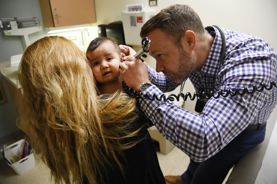 DENVER, CO - JANUARY 25: Physician's assistant Ryan Conrad, right, looks inside the ear canal of patient America Montes, 8-months-old, as her mother Nancy Espino, left, holds her during a well-baby checkup at the Denver Health Sam Sandos Westside Health Center January 25, 2018. (Photo by Andy Cross/The Denver Post via Getty Images)