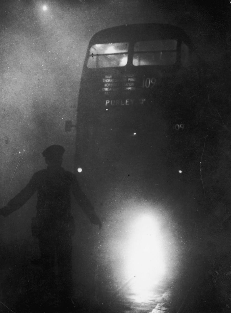 A London bus conductor is forced to walk ahead of his vehicle to guide it through the smog, on December 9, 1952.