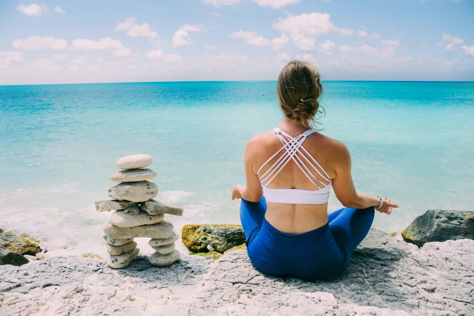 A woman sits meditating in yoga gear while overlooking the ocean in Cayo Largo, Cuba