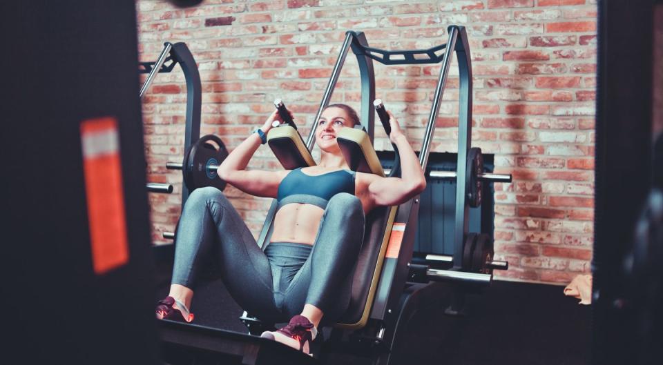 smilling sportswoman doing squatting in training machine at gym leg muscle training