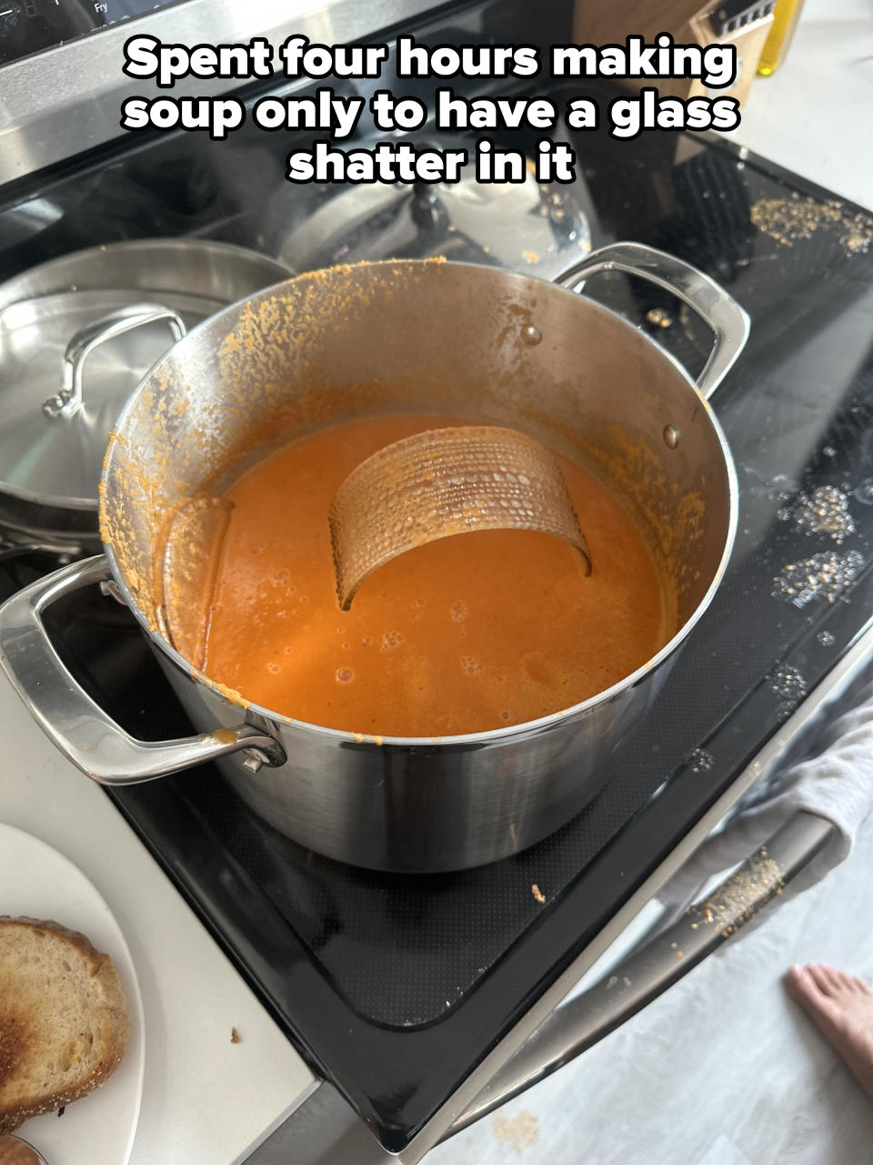 A large metal pot on a stove contains orange soup with part of a metal sieve submerged. Toast is on a plate next to the pot