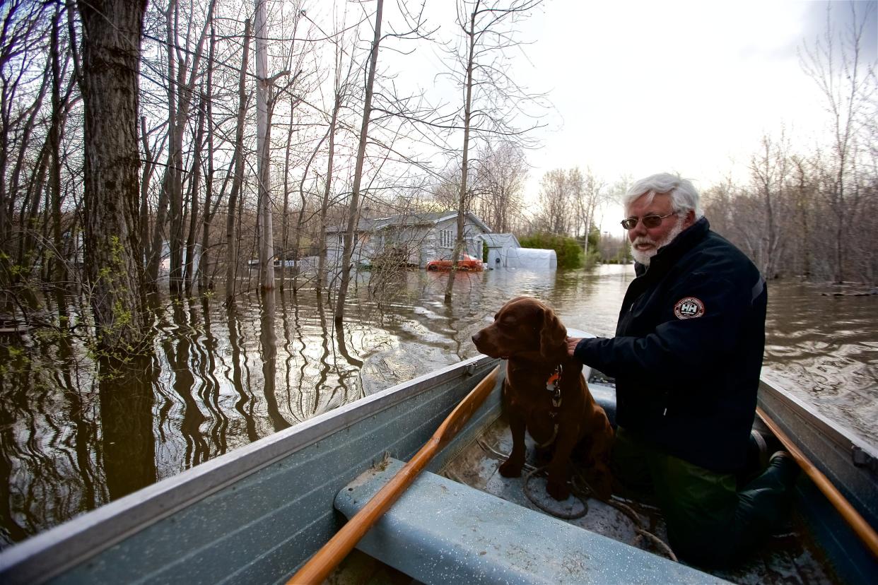 Michel Guerard and his dog Choco return with their boat to help their neighbors to evacuate from their houses affected by floodwaters in Pointe-Calumet, Quebec (The Canadian Press)