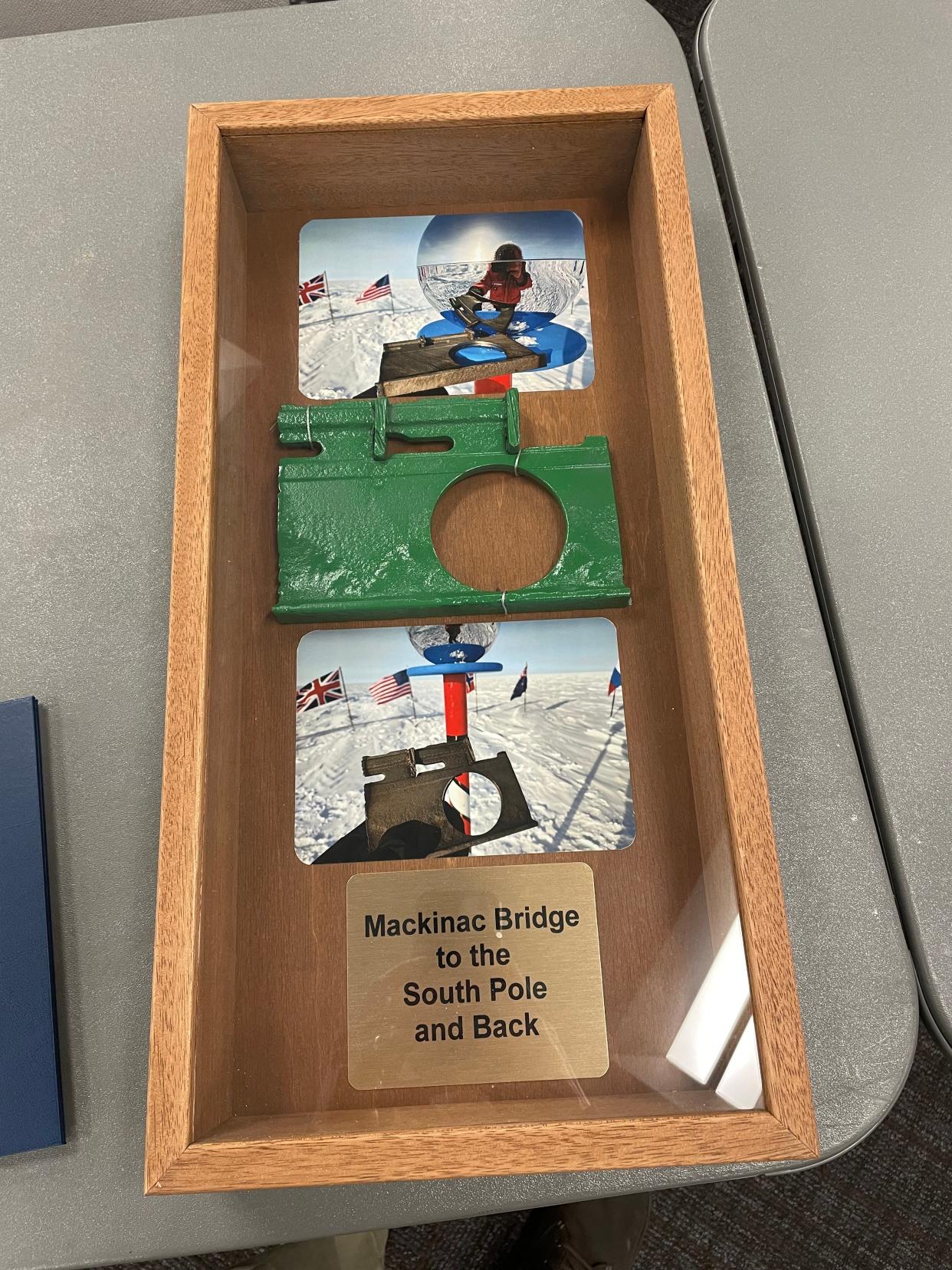 A shadowbox with photos and a piece of the Mackinac Bridge steel used to make the current ceremonial and geographical South Pole markers, presented by Brendan Fisher to the Mackinac Bridge Authority.