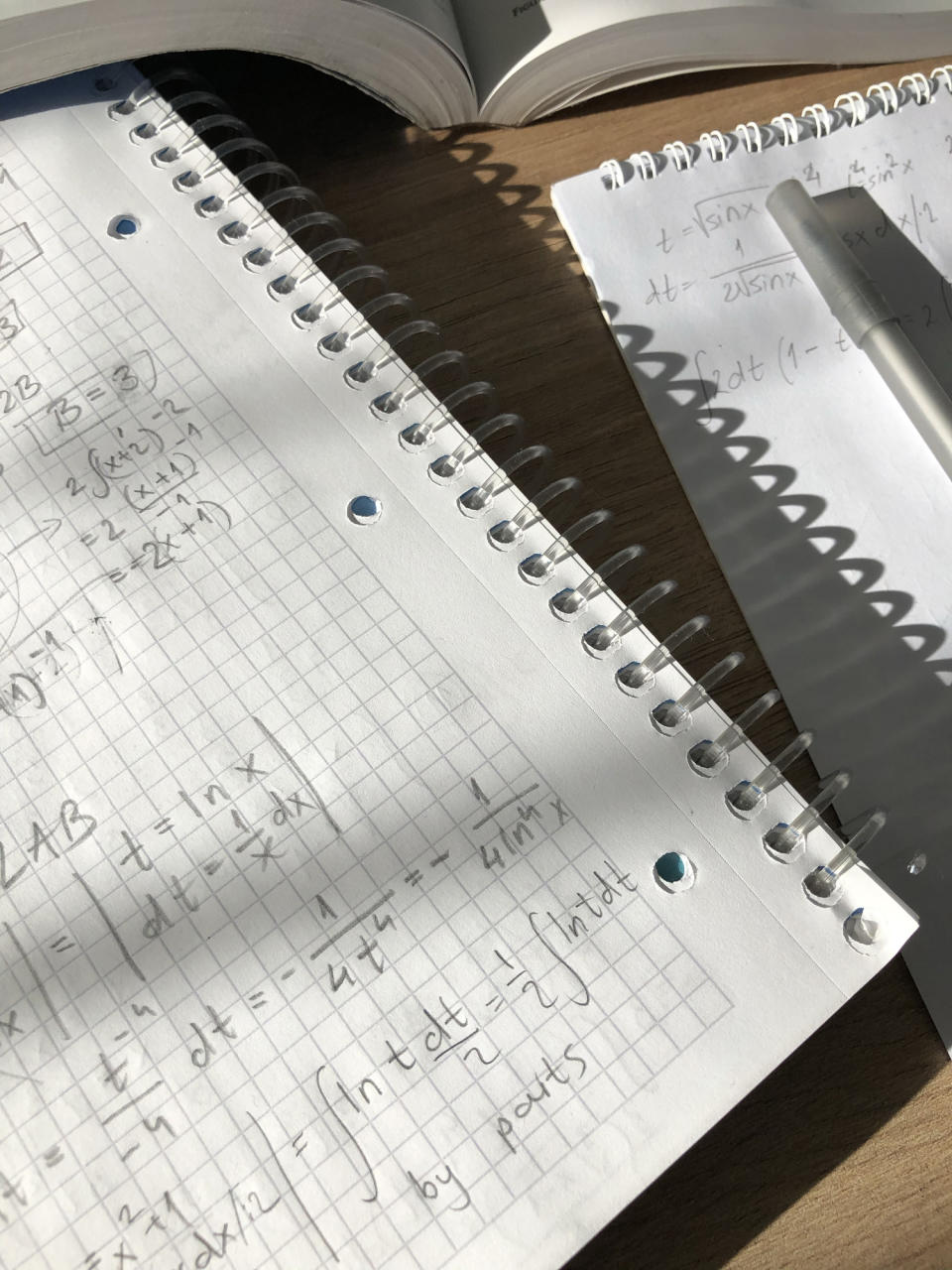 Handwritten mathematical calculations in a notebook with a pen resting on it