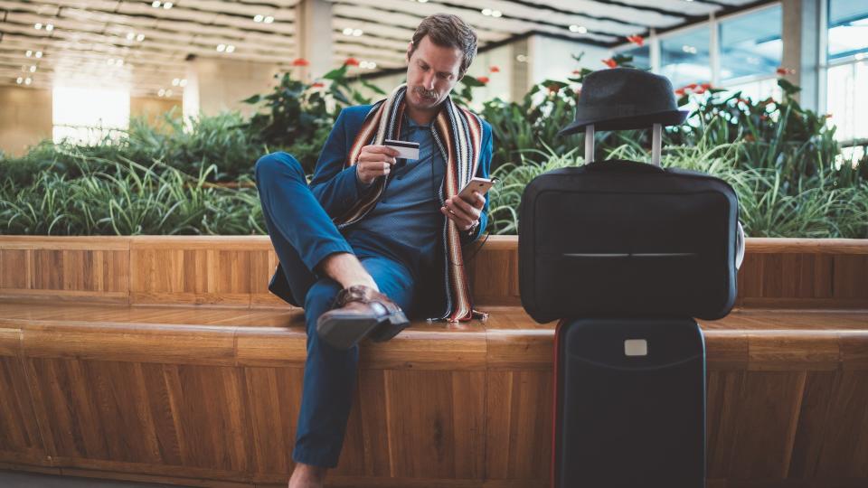 Businessman in casual business clothing using smartphone and credit card for online payments.