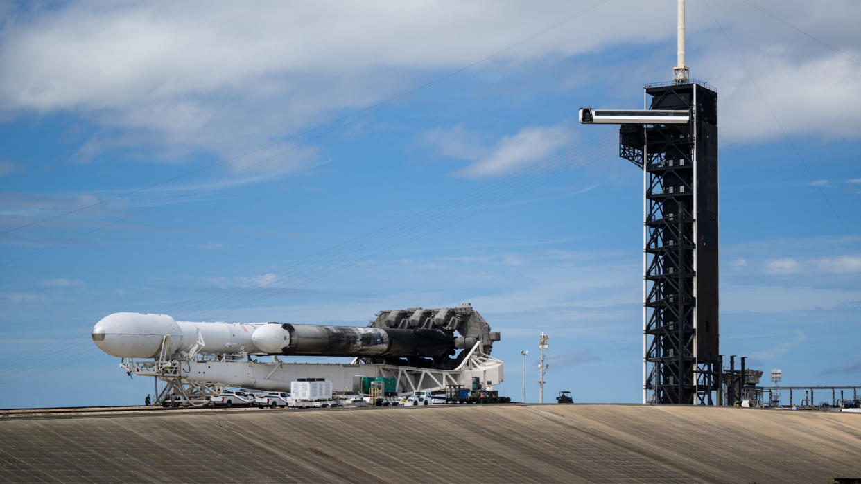  A white spacex falcon heavy rocket is carried horizontally down a track toward the launch pad under a blue sky. 