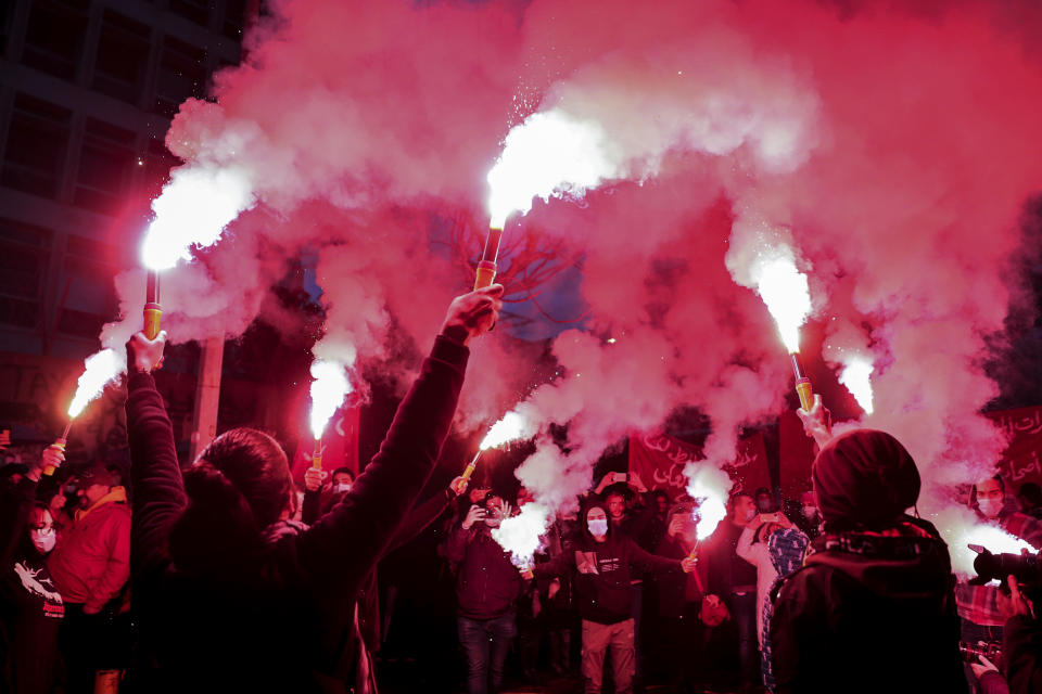 Anti-government protesters hold flares as they chant slogans to denounce the country's deteriorating economic and financial conditions, in front of the Central Bank in Beirut, Lebanon, Sunday, Jan. 23, 2022. (AP Photo/Bilal Hussein)