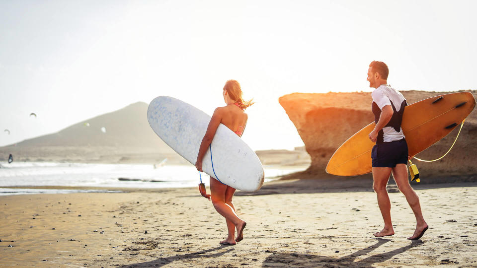 Surfers couple running together with surfboards on the beach at sunset - Sporty friends having fun going to surf - Travel, vacation, sport lifestyle concept.