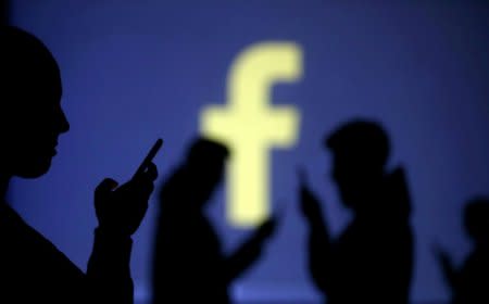 FILE PHOTO: Silhouettes of mobile users are seen next to a screen projection of Facebook logo in this picture illustration taken March 28, 2018.  REUTERS/Dado Ruvic/File Photo