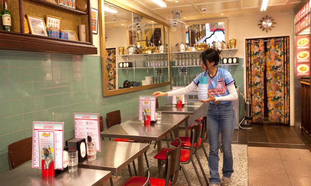 A member of staff carrying dishes and straightening a menu in a brightly lit restaurant 
