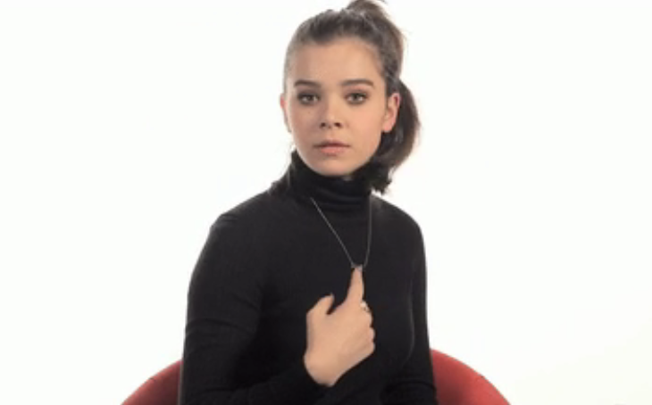 Hailee Steinfeld looking at the camera and pointing to herself as if to say, 