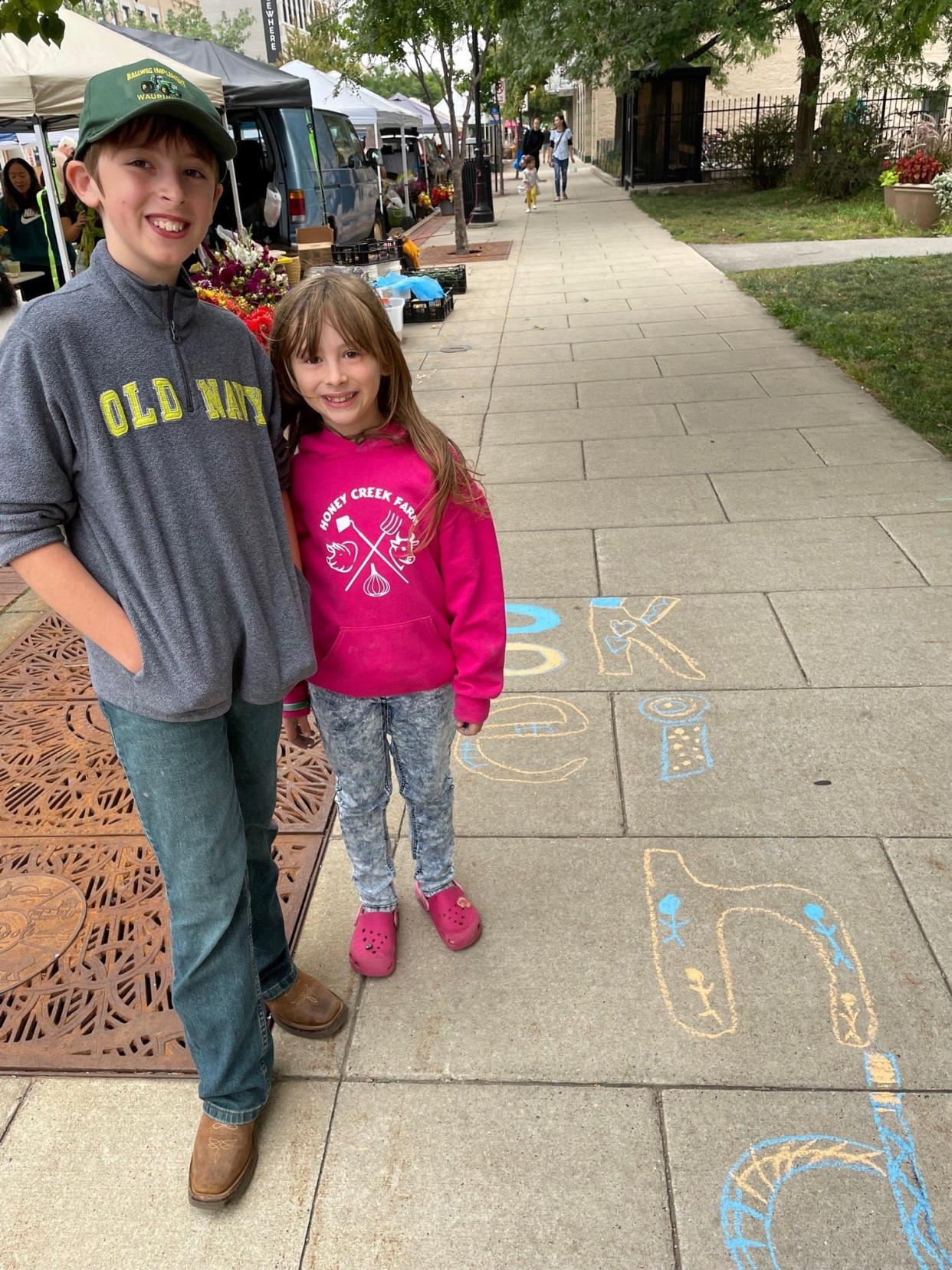 Youth at the Oshkosh Farmers Market show off their chalk art that says, "Be kind." Oshkosh Civility Project team members spoke with attendees over the summer and handed out sidewalk chalk, inviting others to make art.