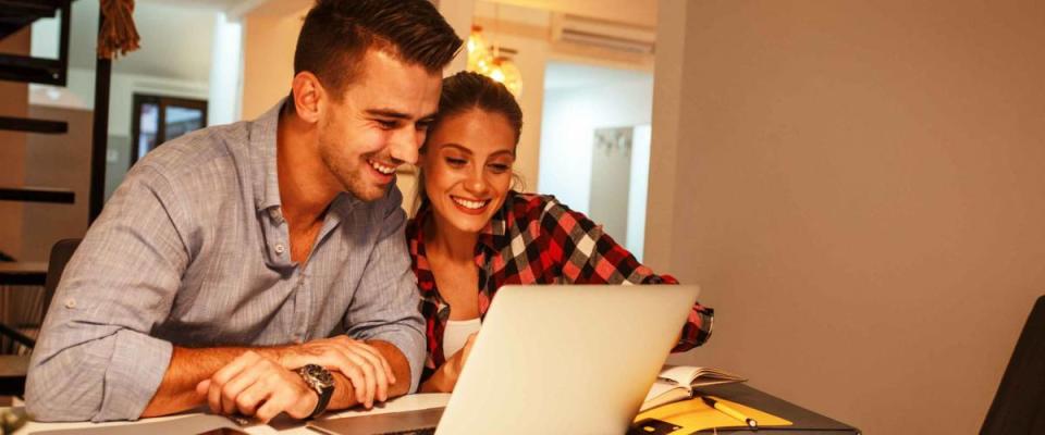 Young married couple sitting at the table in they living room and using laptop.Calculate home budget.