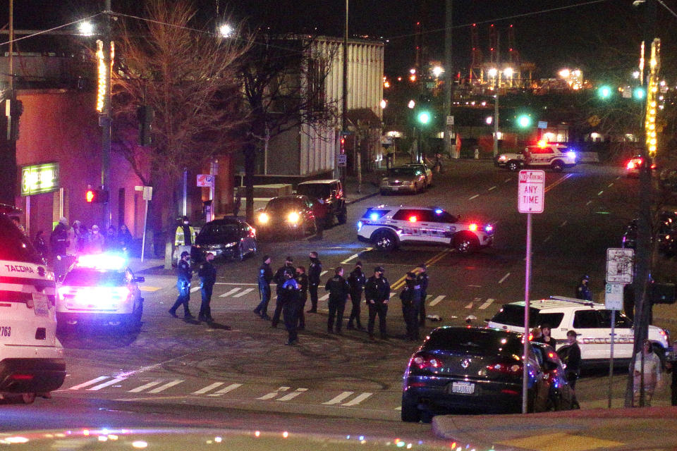 Tacoma Police and other law enforcement officers stand in an intersection near the site of a car crash Saturday, Jan. 23, 2021, in downtown Tacoma, Wash. At least one person was injured when a police car plowed through a crowd of people Saturday night who were watching a downtown street race, the Tacoma News-Tribune reported. (AP Photo/Ted S. Warren)