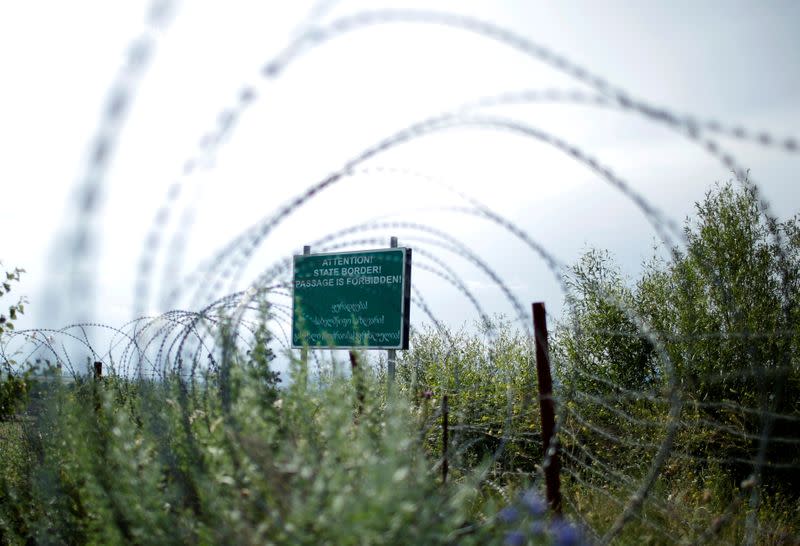 FILE PHOTO: A border sign is seen behind the barbed wire at the de facto border of Georgia's breakaway region of South Ossetia in Khurvaleti