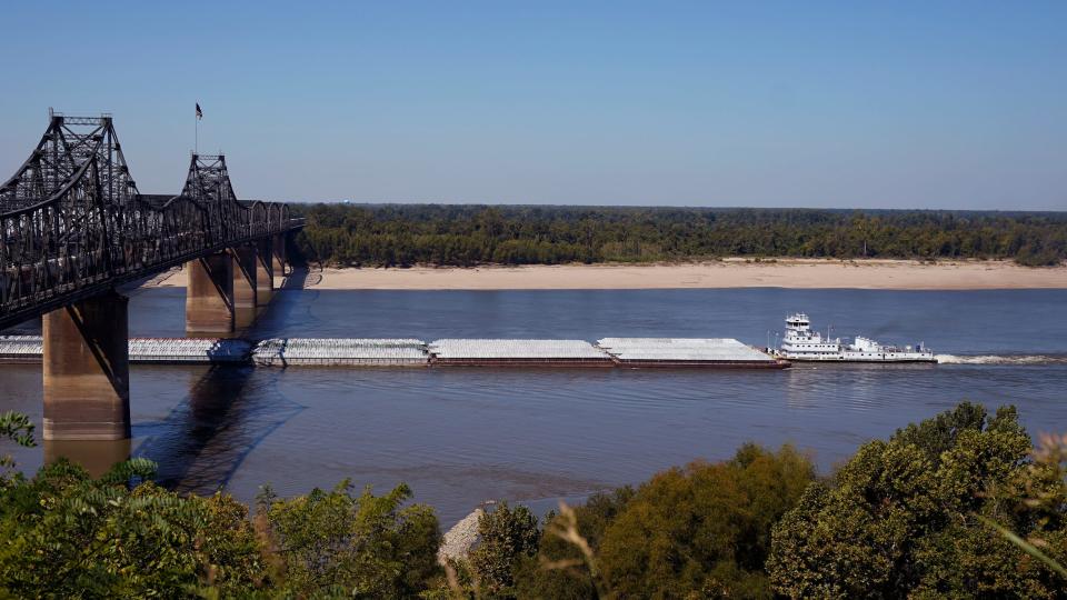 tow trailing five barges floats under bridge in low river waters with exposed dirt banks