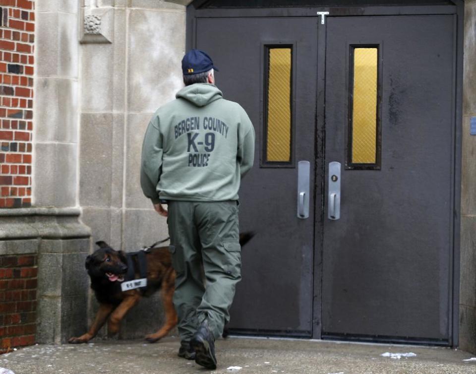 A Bergen County Police officer walks with a police dog outside of Teaneck High School, where at least 60 students were arrested during an overnight break-in, Thursday, May 1, 2014, in Teaneck, N.J. Officers responded to a burglar alarm at the school around 2:30 a.m. Thursday, found urine in the hallways, petroleum jelly on doorknobs, desks flipped over and balloons throughout the building. (AP Photo/Julio Cortez)