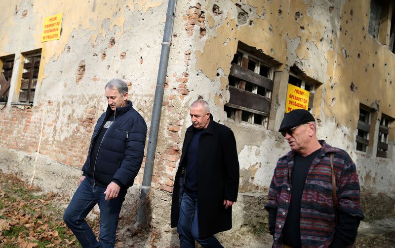 War veterans Boro Jevtic (L-R), Marko Zelic and Rizo Salkic walk past a house destroyed during the Bosnian War in Maglaj