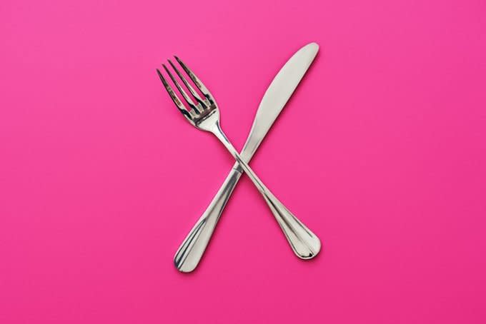 Knife and fork crossed, isolated on pink background