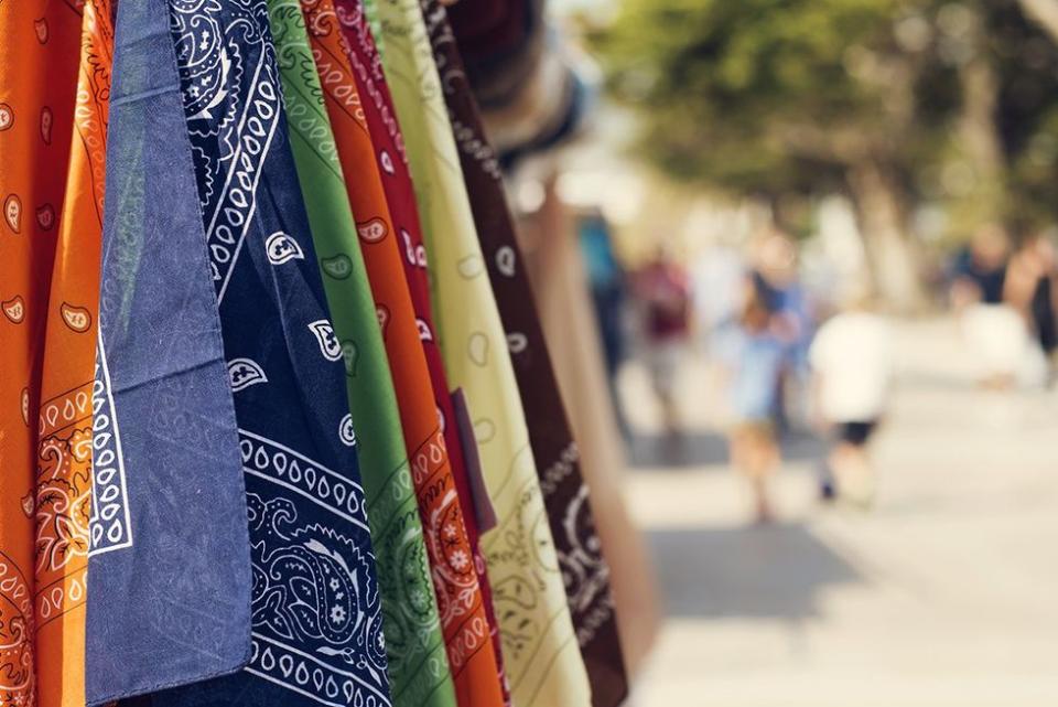 some paisley patterned kerchiefs of different colors on sale hanging on a rack in the street