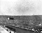 <p>Distance runner Paavo Nurmi and Hannes Kolehmainen, known as "The Flying Finns," light two seperate cauldrons. Thousands of carrier pigeons are released to start the Games.</p>
