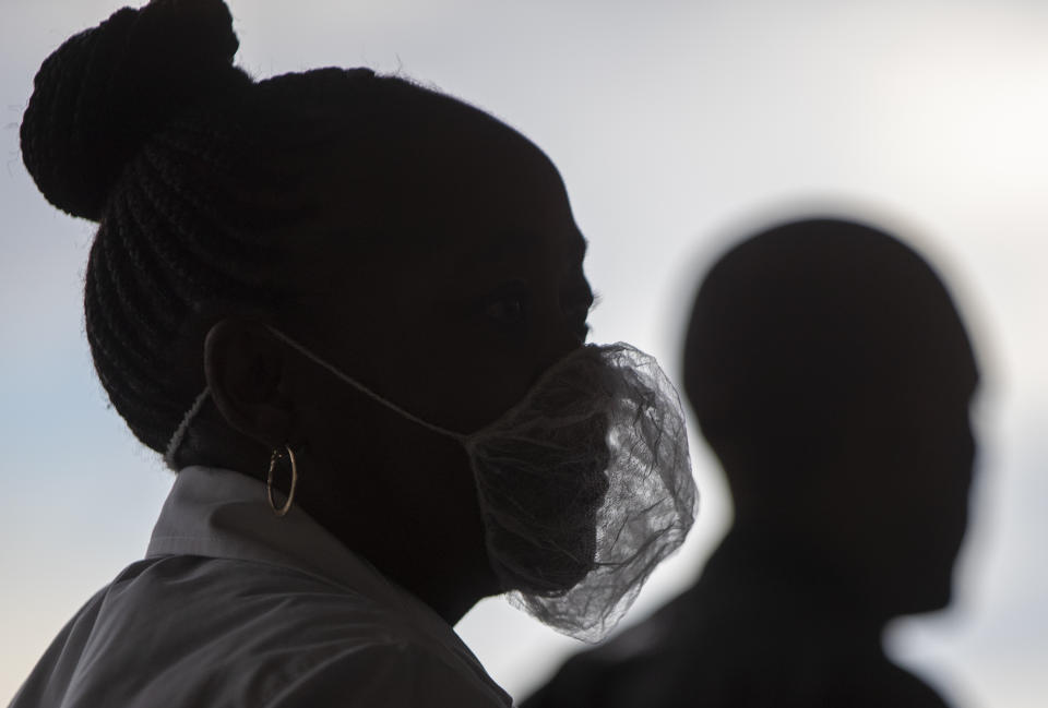A woman wearing a disposable white beard mask, to protect against coronavirus, stands outside the entrance of a shopping supermarket in Soweto, South Africa, Thursday, March 26, 2020. In just hours, South Africa goes into a nationwide lockdown for 21 days, in an effort to mitigate the spread to the coronavirus. (AP Photo/Themba Hadebe)