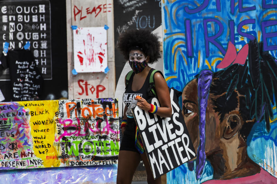 A marcher walks past banners and signs at Black Lives Matter Plaza near the White House in Washington, during the March on Washington, Friday, Aug. 28, 2020, commemorating the 57th anniversary of the Rev. Martin Luther King Jr.'s "I Have A Dream" speech. (AP Photo/Manuel Balce Ceneta)