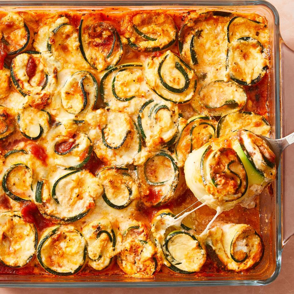 zucchini slices rolled up around cheese with sauce in a casserole dish