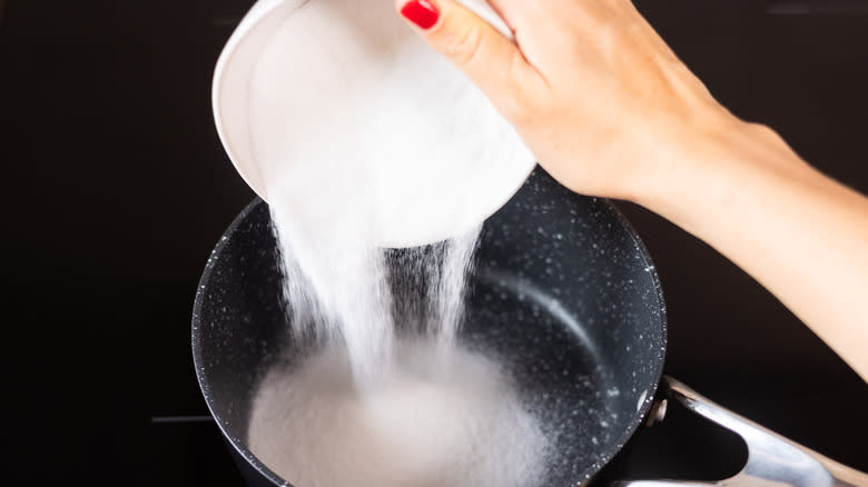 hand pouring sugar into saucepan