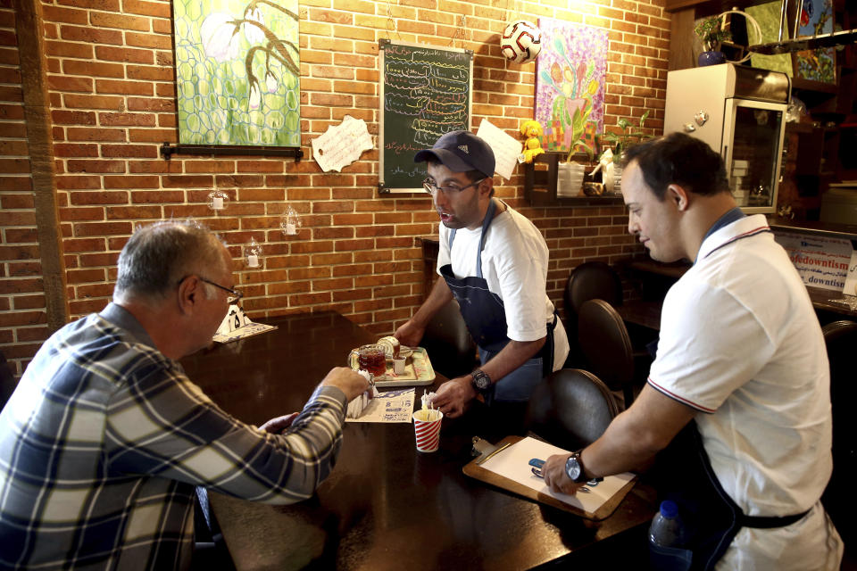 In this Monday, Aug. 6, 2018, photo, two cafe staffers, Mehdi Khakian, with autism, center, and his colleague Iman Arbabi, with down syndrome, right, work in Downtism Cafe in Tehran, Iran. The popular cafe in Tehran’s bustling Vanak Square, whose name combines “Down” with “autism,” is entirely run by people with Down syndrome or autism. More than just providing meaningful work, the cafe is helping break down barriers by highlighting how capable people with disabilities are. (AP Photo/Ebrahim Noroozi)