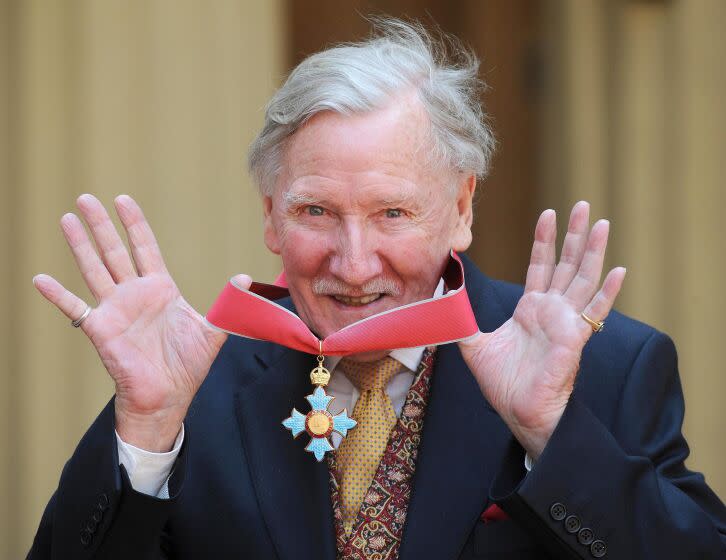 A man with gray hair smiling in a suit and holding a red ribbon around his neck