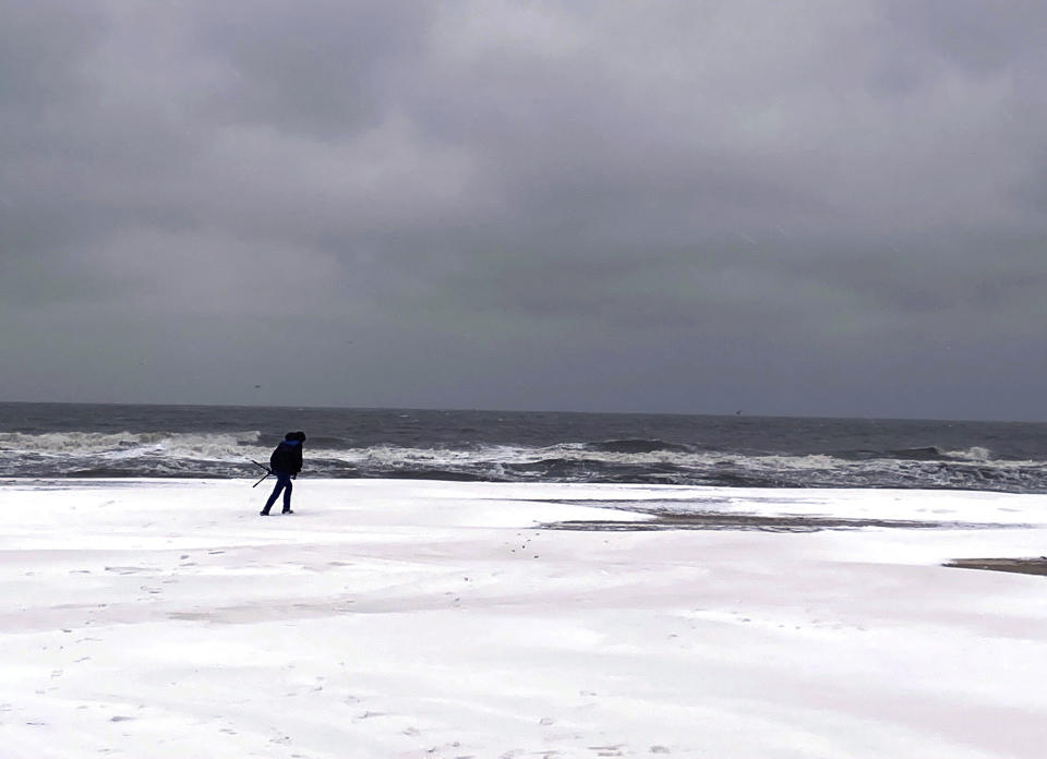 A person walks along the Virginia Beach oceanfront covered in snow, Saturday, Jan. 22, 2022. A layer of ice and a blanket of snow has covered coastal areas stretching from South Carolina to Virginia. The winter weather system that entered the region on Friday brought colder temperatures and precipitation not often seen in the region. (Stacy Parker/The Virginian-Pilot via AP)