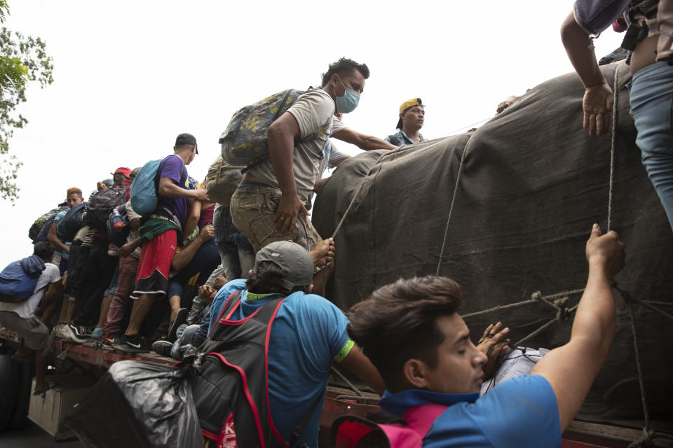 Migrants climb on to the back of a freight truck that slowed down to give them an opportunity to jump on in Rio Dulce, Guatemala, Friday, Oct. 2, 2020. A new caravan of about 2,000 migrants set out from neighboring Honduras in hopes of reaching the United States. (AP Photo/Moises Castillo)