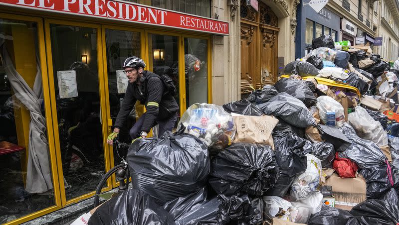 A cyclist rides past an uncollected garbage pile next to the cafe “The President” in Paris, Tuesday, March 21, 2023. Garbage collectors are on strike over a bill pushed through by President Emmanuel Macron without lawmakers’ approval still faces a review by the Constitutional Council before it can be signed into law. Meanwhile, oil shipments in the country were disrupted amid strikes at several refineries in western and southern France.
