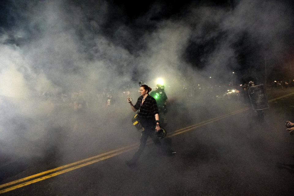 A woman walks through smoke during the 100th consecutive day of demonstrations in Portland, Ore., as police use chemical irritants and crowd control munitions to disperse protesters on Saturday, Sept. 5, 2020.(AP Photo/Noah Berger)