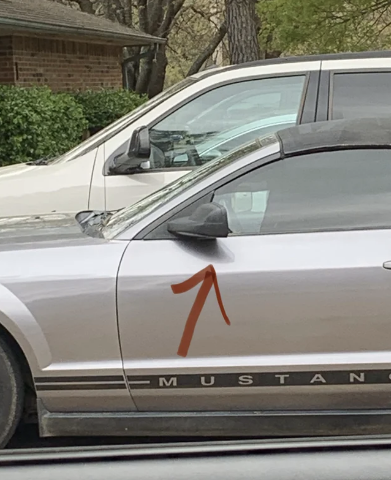 A mustang car with dark tints on the driver's side window. There is a hole cut out so that the driver can see the side mirror while they drive