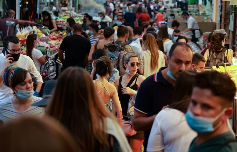 Shoppers, some wearing face masks against the coronavirus, crowd an alley of Jerusalem's main market.