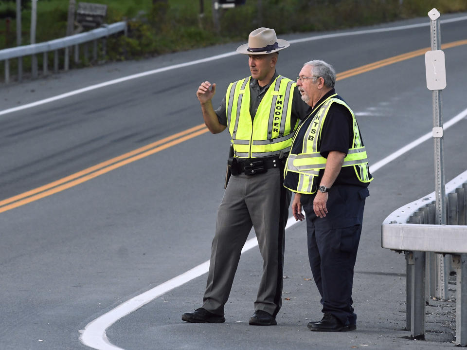 A New York state trooper and a member of the National Transportation Safety Board view the scene of Saturday's fatal crash in Schoharie, N.Y., Sunday, Oct. 7, 2018. A limousine loaded with revelers headed to a 30th birthday party blew a stop sign at the end of a highway and slammed into an SUV parked outside a store, killing all people in the limo and a few pedestrians, officials and relatives of the victims said Sunday. (AP Photo/Hans Pennink)