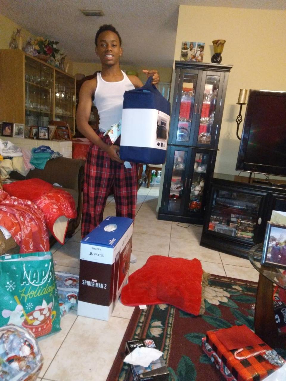 John Deandre, de 13 años, es criado por sus bisabuelos Evie y Rupert Lounges en Lauderdale Lakes. La foto de muestra algunos de los regalos navideños, entre ellos un PlayStation, un juego de edredón y ropa, que recibió este año de los donantes de Wish Book.