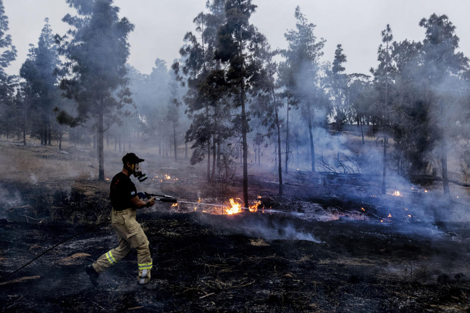 An Israeli firefighter attempts to extinguish a fire caused by an incendiary balloon launched by Palestinians from the Gaza Strip, on the Israeli Gaza border, Sunday, May 9, 2021. Protest groups affiliated with Gaza's militant Hamas rulers began launching the incendiary balloons to protest what they say are heavy-handed Israeli actions at the Al-Aqsa mosque and elsewhere in Jerusalem in recent days. Hamas had largely curtailed launches of the balloons over the past two years as part of an informal cease-fire. (AP Photo/Tsafrir Abayov)