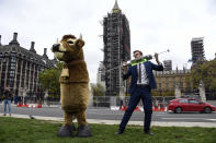 A man imitates the injection of hormones into a man in a cow costume, in Parliament Square, as part of a day of action against the US trade deal, ten days before the US Presidential election, in London, Saturday, Oct. 24, 2020. There will will be protests held nationwide against a proposed US trade deal, opposed by a number of organisations including Global Justice Now and Stop Trump Coalition. (AP Photo/Alberto Pezzali)
