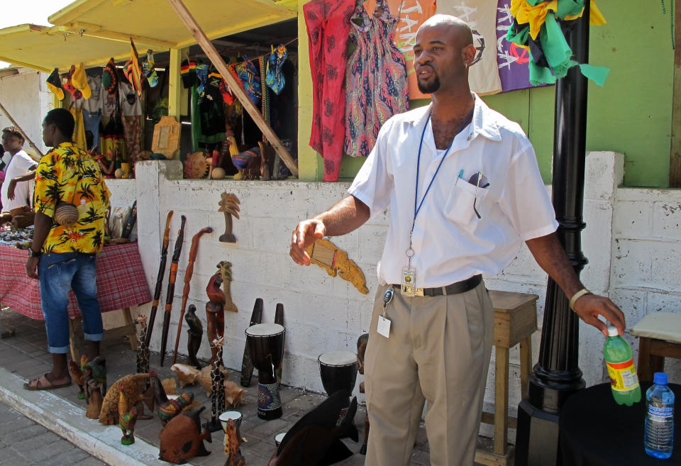 In this Sept. 26, 2012 photo, street vendor Paul Davy sells wooden statues to tourists who disembarked from the Royal Caribbean's Allure of the Seas cruise ship in Falmouth, northern Jamaica. Trade groups say the flourishing cruise ship industry injects about $2 billion a year into the economies of the Caribbean, the world’s No. 1 cruise destination, but critics complain that it produces relatively little local revenue because so many passengers dine, shop and purchase heavily marked-up shore excursions on the boats or splurge at international chain shops on the piers. (AP Photo/David McFadden)