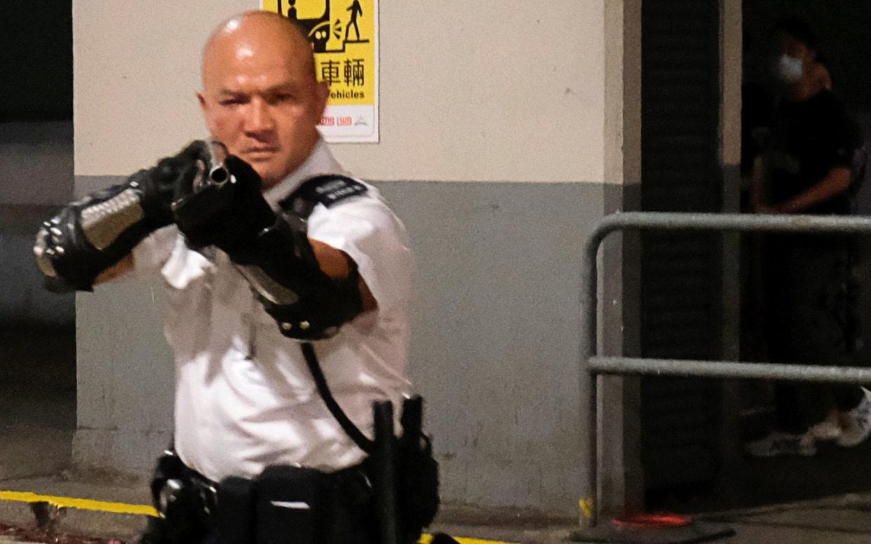 A police officer points a gun towards anti-extradition bill protesters who surrounded a police station where detained protesters are being held during clashes in Hong Kong - REUTERS