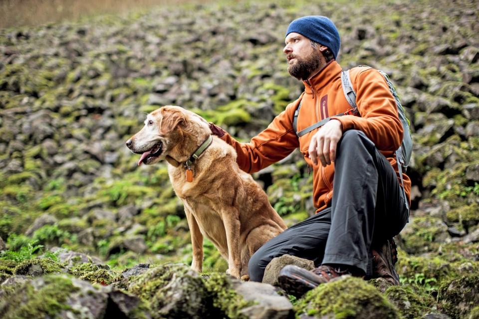 man petting his Labrador retriever on a hike on a rocky hill